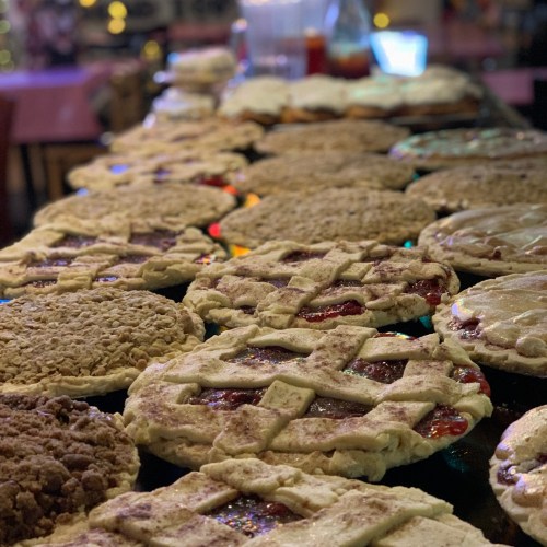 A variety of freshly baked pies with lattice crusts, displayed on a table, showcasing different flavors and toppings.
