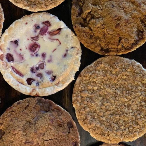 A variety of baked goods, including a cherry pie and crumbly cookies, arranged on a wooden surface.