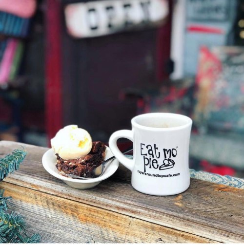 A mug with "Eat mo' pie" and a plate of brownie topped with ice cream on a wooden surface.