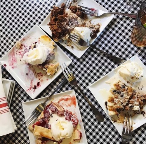 Four plates of dessert with ice cream, partially eaten, on a checkered tablecloth. Forks scattered around.