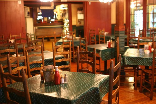 A cozy restaurant interior with wooden chairs and tables, featuring green tablecloths and condiments on the tables.