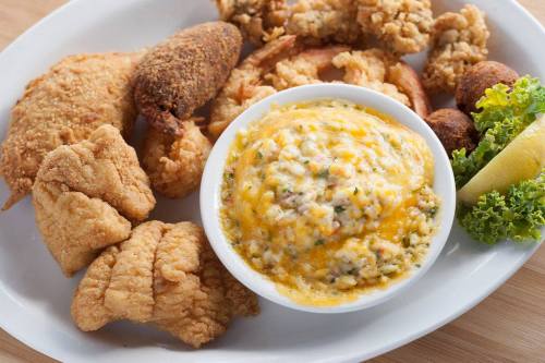 A plate of fried fish, shrimp, hushpuppies, and a bowl of cheesy grits, garnished with lettuce and a lemon wedge.
