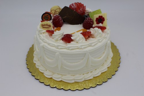 A round white cake decorated with strawberries, raspberries, chocolate, and colorful toppings on a gold platter.