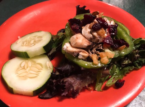 A colorful salad on a red plate, featuring greens, cucumber slices, mushrooms, and dried cranberries.