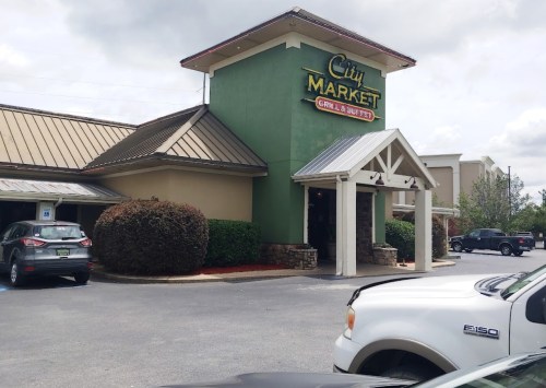 Exterior of City Market Grill & Buffet, featuring a green and tan building with a peaked roof and parking area.