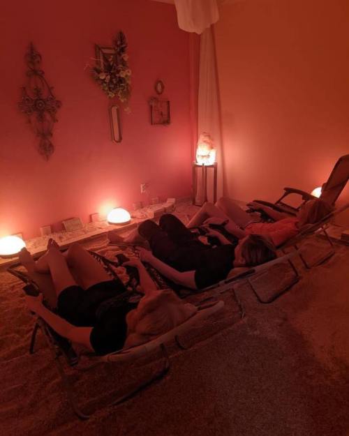 Three people relax on lounge chairs in a softly lit room with orange walls and salt lamps, creating a calming atmosphere.