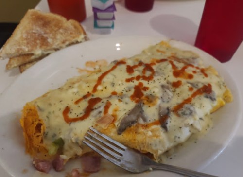 A large omelette topped with cheese and sauce, served with toast on the side.