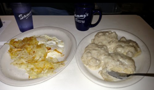 A plate with hash browns, two eggs, and biscuits smothered in gravy, alongside a blue mug labeled "Sammy's."