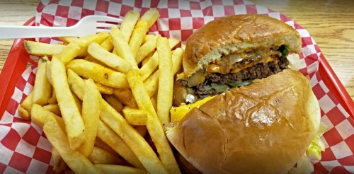 A juicy cheeseburger with lettuce and onions, served with a side of golden French fries on a red checkered tray.