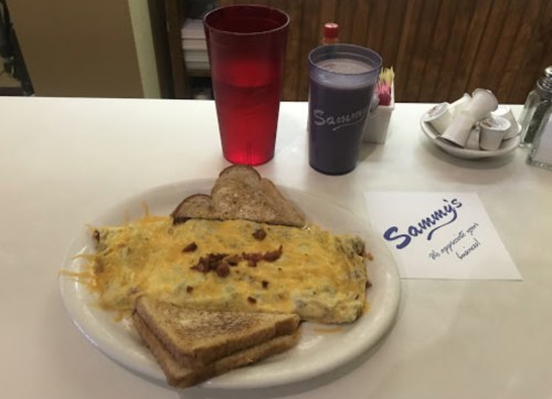 A plate with a cheesy omelet, toast, and drinks at Sammy's diner, with a sign reading "We appreciate your business!"