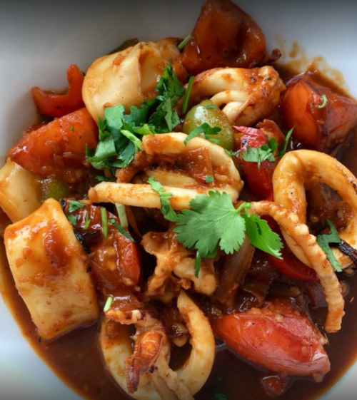 A close-up of a colorful seafood dish featuring squid, bell peppers, and herbs in a rich sauce.