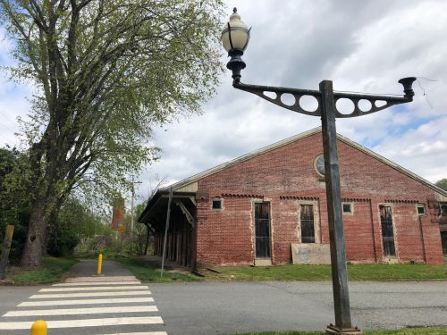A brick building with large windows, a streetlamp, and a tree beside a crosswalk under a cloudy sky.
