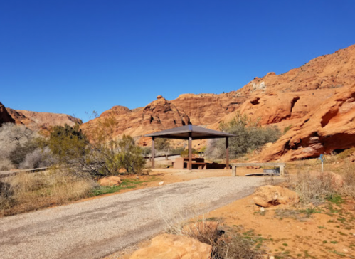A shaded picnic area with a wooden shelter surrounded by red rock formations and clear blue skies.