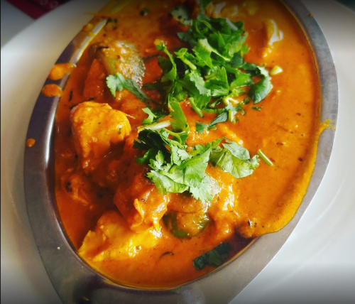 A silver dish filled with creamy orange curry topped with fresh cilantro and pieces of chicken.