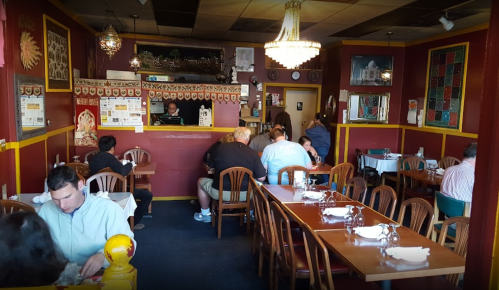 A cozy restaurant interior with wooden tables, patrons dining, and a counter in the background. Warm, inviting decor.