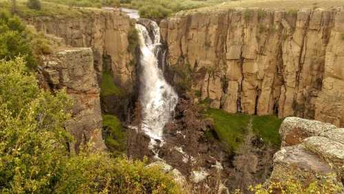 A stunning waterfall cascades down rocky cliffs, surrounded by lush greenery and rugged terrain.