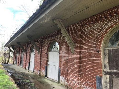 A brick building with arched windows and wooden doors, featuring decorative wooden supports along the roofline.