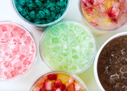 A variety of colorful drinks in clear cups filled with ice, featuring shades of red, green, and brown.