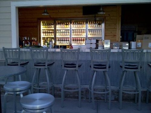 A bar with high stools and a display of various bottles in a wooden setting.