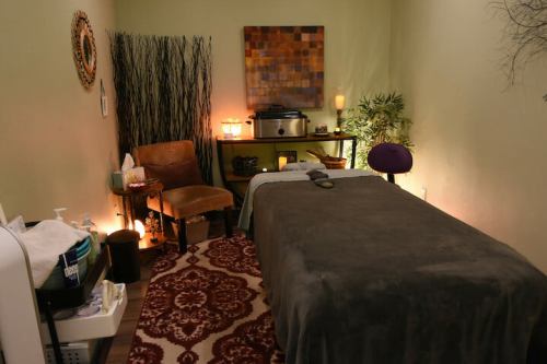 A serene spa room with a massage table, cozy chair, soft lighting, and calming decor.