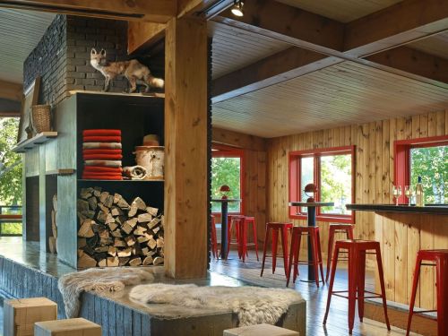 Cozy interior featuring wooden beams, a stacked fireplace, red accents, and modern bar stools in a warm, inviting space.