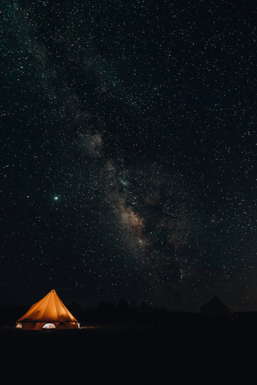 A glowing orange tent under a starry night sky, with the Milky Way visible in the background.
