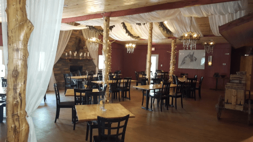 Cozy restaurant interior with wooden tables, black chairs, draped fabric, and decorative lighting.