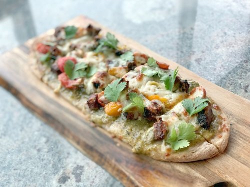 A flatbread pizza topped with cheese, colorful tomatoes, and fresh cilantro, served on a wooden board.