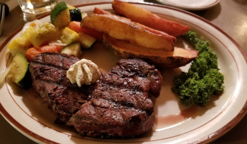 A plate featuring a grilled steak with a dollop of butter, potato wedges, and mixed vegetables.