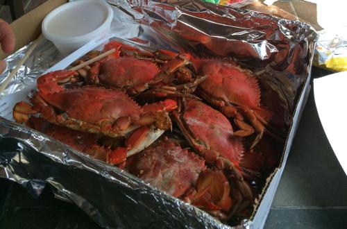 A tray of cooked crabs, covered in foil, with a small container on the side.