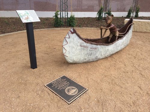 A sculpture of a figure paddling a canoe, accompanied by informational plaques in a landscaped area.