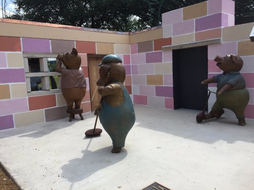 Three whimsical pig sculptures in a colorful, partially constructed building, each engaged in different activities.