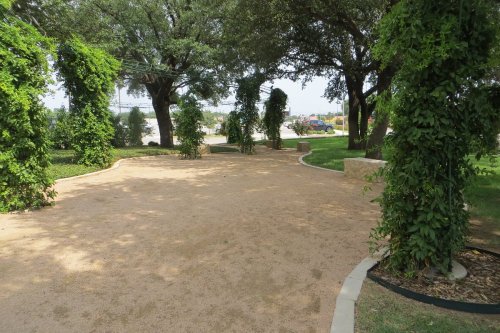 A sandy pathway lined with lush greenery and trees, leading through a serene outdoor space.