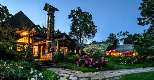 A charming lodge surrounded by lush greenery and colorful flowers, illuminated at dusk.