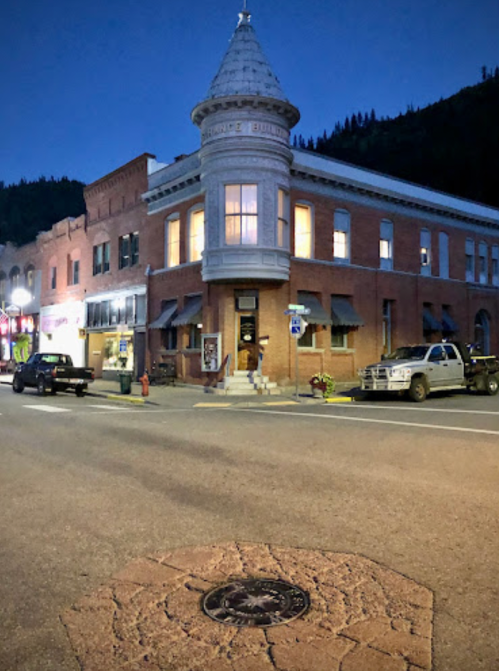 Historic brick building with a turret, streetlights, and parked cars at dusk.