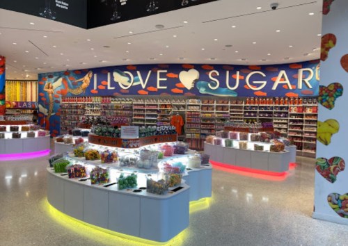Colorful candy store interior with vibrant "I LOVE SUGAR" mural and shelves filled with various sweets and treats.