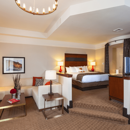 A cozy hotel room featuring a bed, seating area, and warm lighting, with modern decor and a chandelier overhead.