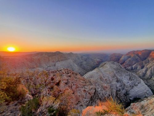 A stunning sunset over rugged mountains, casting warm hues across the landscape and valleys below.
