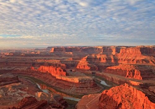 A stunning view of red rock formations and a winding river under a cloudy sky in a canyon landscape.