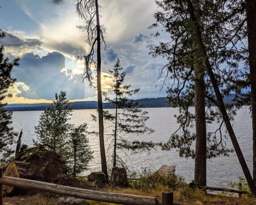 A serene lakeside scene with trees framing the water, under a cloudy sky at sunset.