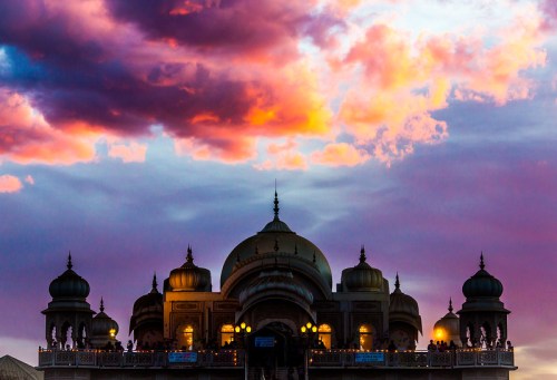 Silhouette of a grand building with domes against a vibrant sunset sky filled with colorful clouds.