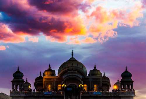 Silhouette of a grand building with domes against a vibrant sunset sky filled with colorful clouds.