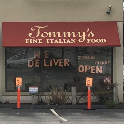 Sign in a restaurant window reads "Tommy's Fine Italian Food," with "WE DELIVER" and "CURBSIDE PICK UP OPEN."