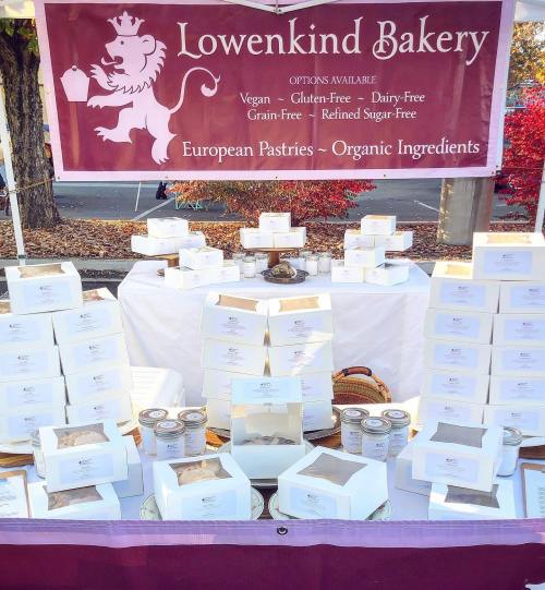 A bakery stall displaying various pastries in white boxes, with a sign highlighting vegan and organic options.
