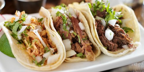 Three delicious tacos filled with shredded chicken, beef, and fresh toppings, served on a white plate with lime.