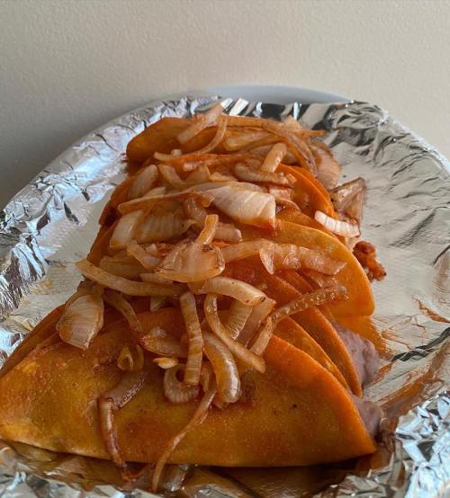 A plate of tacos topped with sautéed onions, served on aluminum foil.
