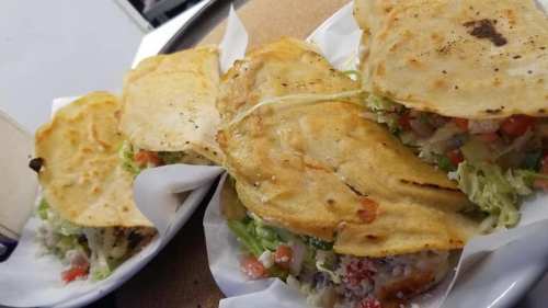 Three crispy tacos filled with fresh vegetables and toppings, served on a white plate.