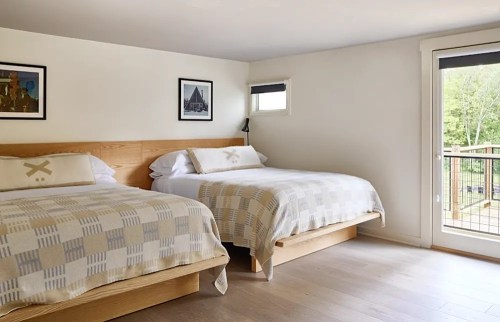 A cozy hotel room with two beds, light-colored bedding, and a balcony door leading to an outdoor view.