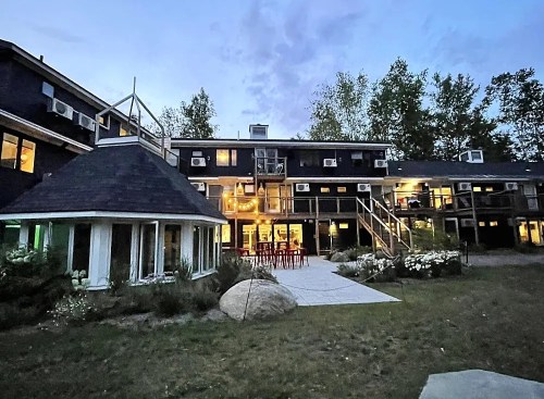 A modern building with multiple levels, surrounded by greenery and outdoor seating, under a twilight sky.