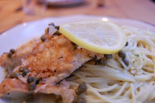 A plate of lemon-butter fish served over spaghetti, garnished with capers and a slice of lemon.